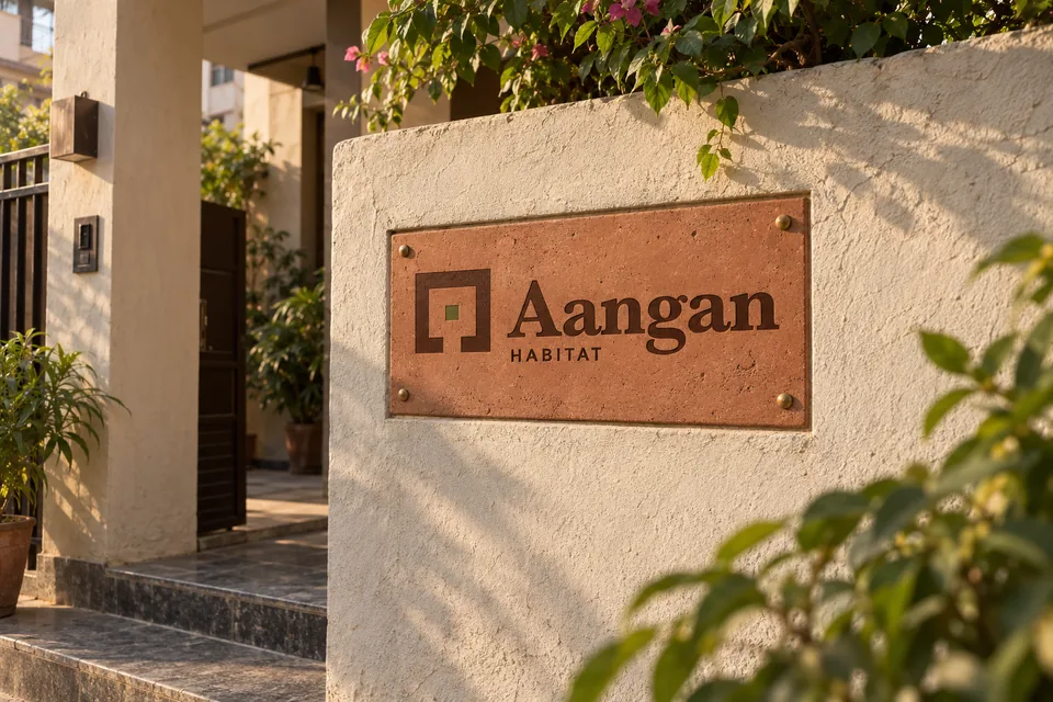 Late-afternoon editorial photograph of a tactile terracotta and stone Aangan Habitat entry plaque in a modest Indian residential setting.